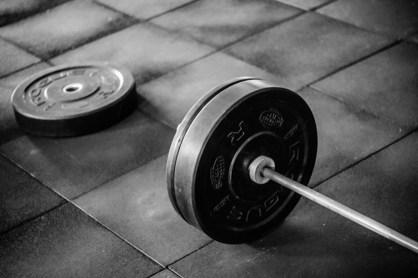 Loaded barbell plate on a gym floor next to a spare weight plate, representing progressive overload training