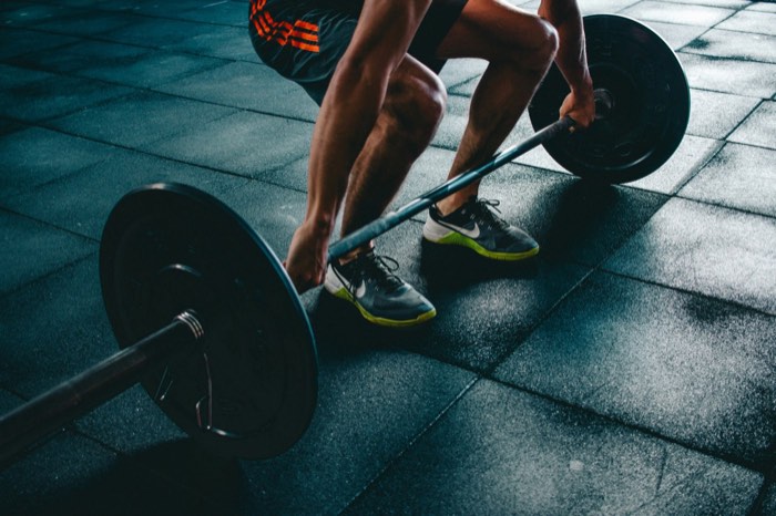 Lifter gripping a loaded barbell in a deadlift setup, part of a push pull legs (PPL) routine